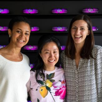 Three EDF Climate Corps fellows standing in front of a wall with light-up Lyft logos.